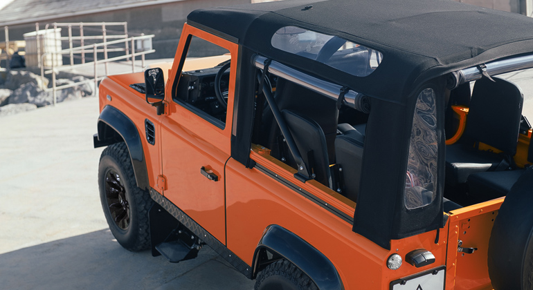 Side view of orange Defender 90 soft-top on the beach