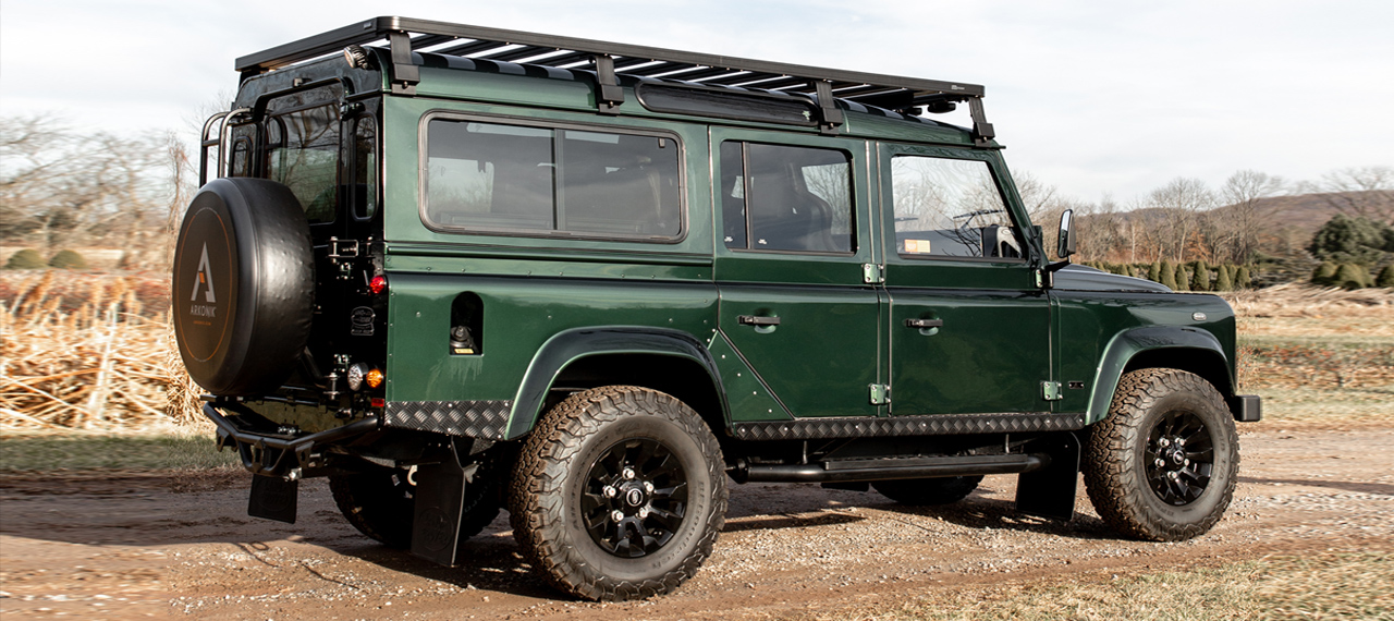 Side view of green Land Rover Defender on dirt track