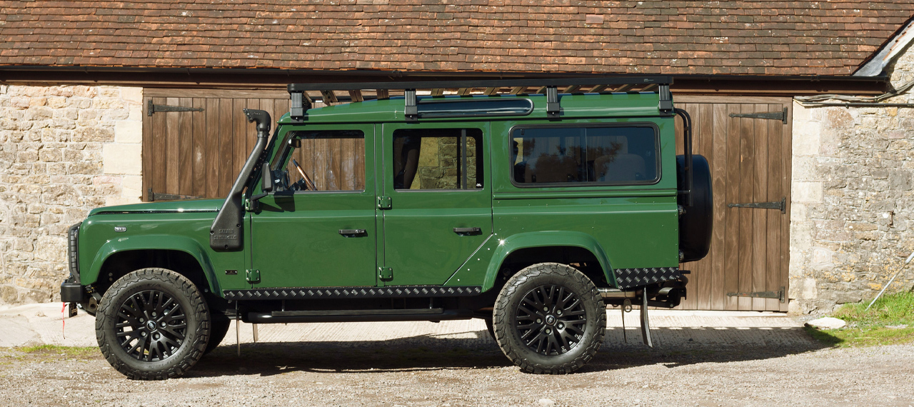 Side view of Coniston Green Defender with wading kit in front of barn