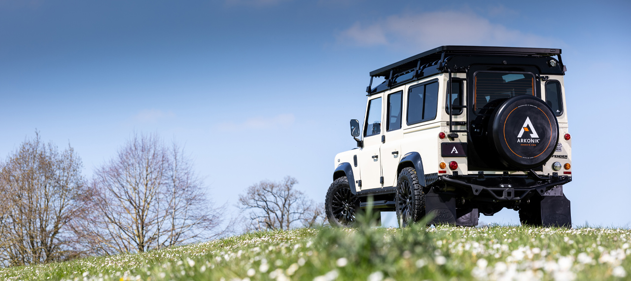 Rear view of a Limestone Beige and Black Arkonik Defender in field with blue sky