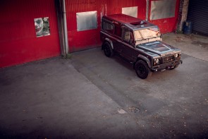 Arkonik Land Rover Defender parked next to red factory doors.