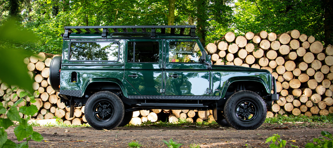 Side view of Epsom Green Arkonik Defender 110 in front of logpile